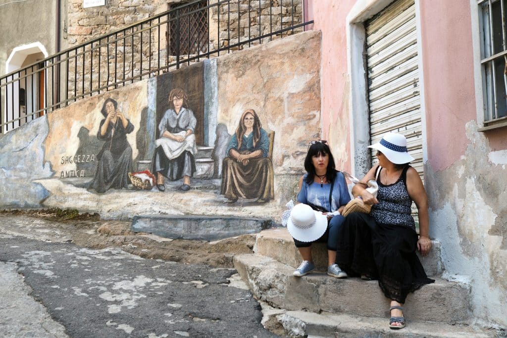 Murales a ženy sedící na chodníku v Orgosolu na Sardinii