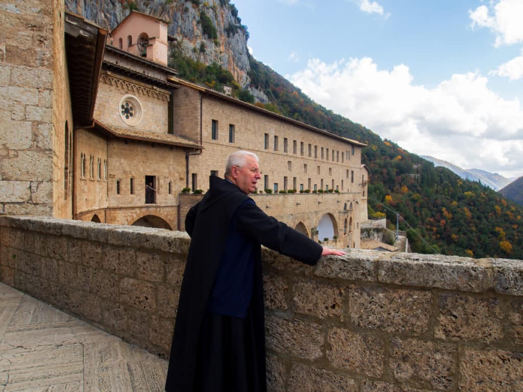 Mnich vyhlíží přes zábradlí v klášteře sv. Benedikta,někdy nazývaném podle jeskyně sv. Benedikta rovněž Sacro Speco