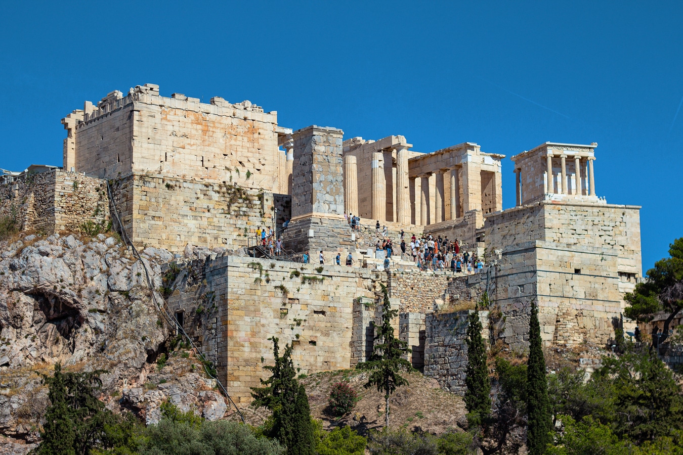 Pohled od Areopagu na monumentální vstup (propylaje) na Akropoli, vpravo na mohutném podstavci stojí malý chrám Athény Níké (se čtyřmi iónskými sloupy v průčelí), zcela vlevo je tzv. pinakotéka a před ní vysoký podstavec památníku, jemuž se říká Agrippův